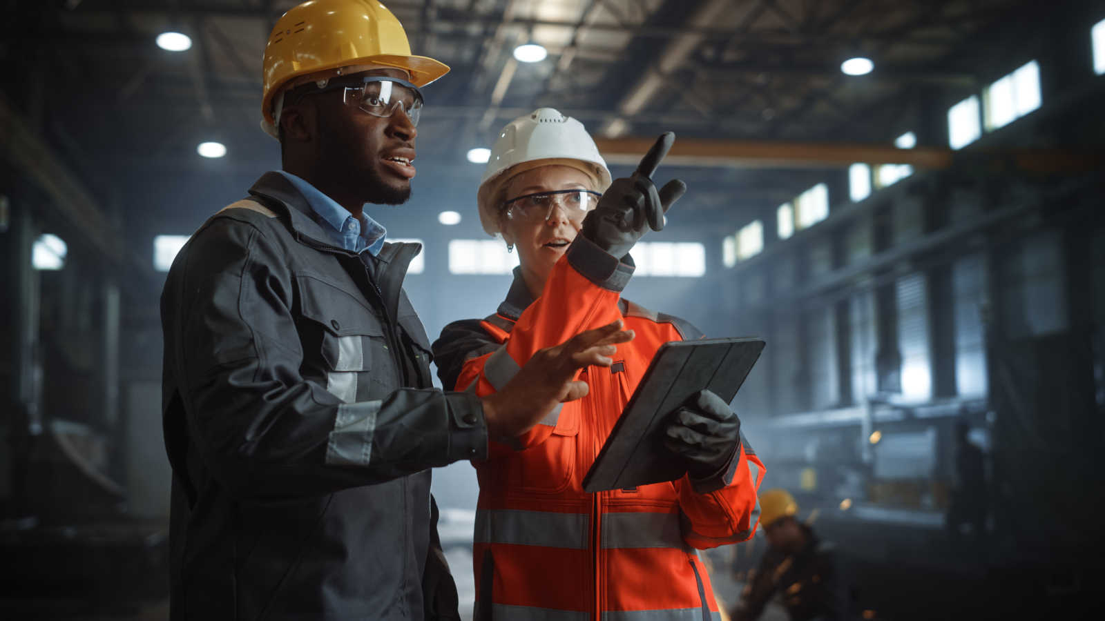 Two Heavy Industry Engineers Stand in Steel Metal Manufacturing Factory, Use Digital Tablet Computer and Have a Discussion. Black African American Industrial Specialist Talk to Female Technician.