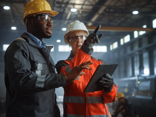 Two Heavy Industry Engineers Stand in Steel Metal Manufacturing Factory, Use Digital Tablet Computer and Have a Discussion. Black African American Industrial Specialist Talk to Female Technician.